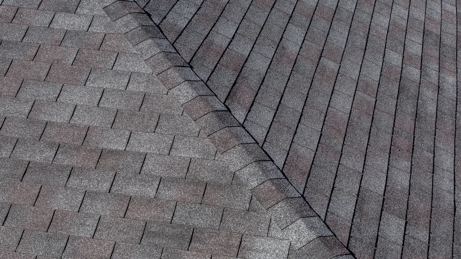 Gray three-tab asphalt shingle slopes crossed by a hip ridge line
