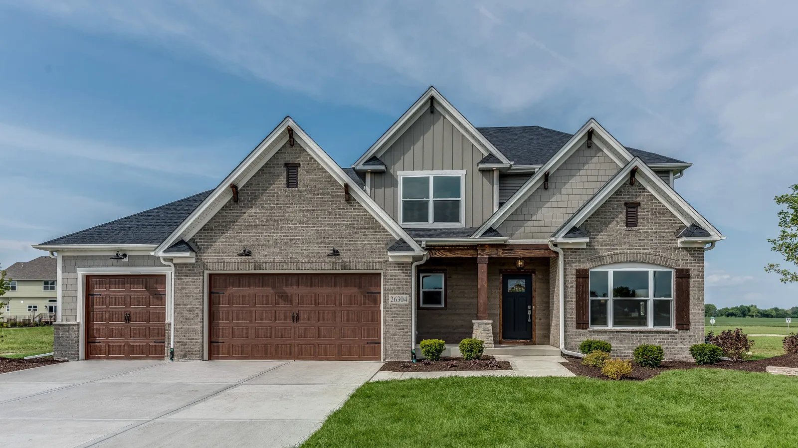 Wood garage doors and a dark shingle roof on a gray brick craftsman home