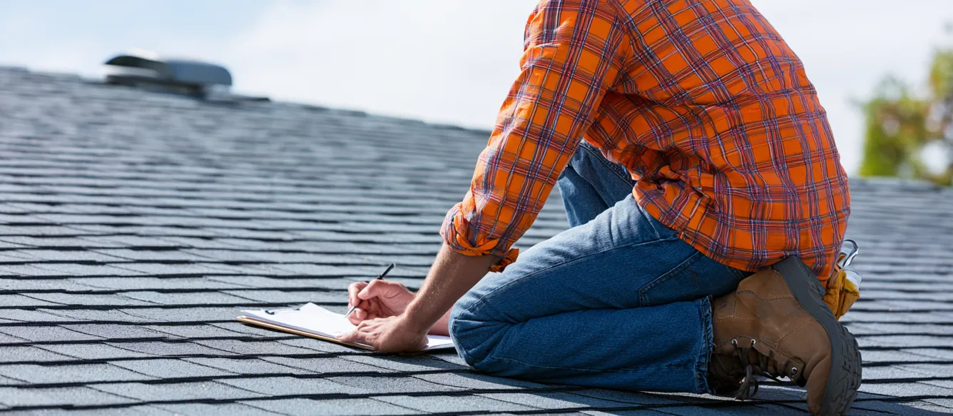 Gray shingle roof with an inspector writing on a clipboard